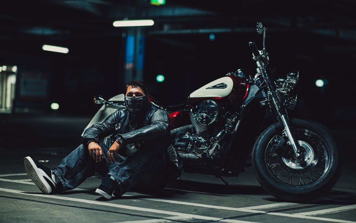 Motocyklista w skórzanej kurtce klęczący przy motocyklu w słabo oświetlonym garażu