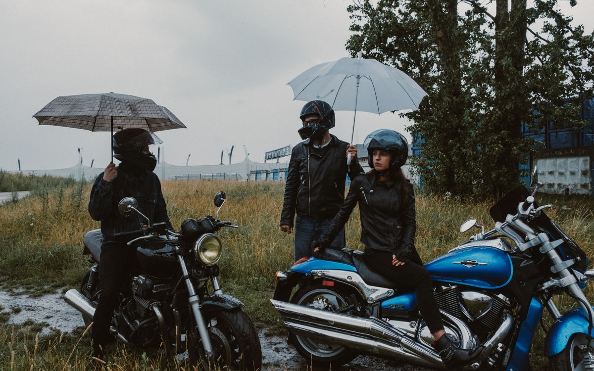 Motocykliści chroniący się przed deszczem pod parasolami na trawiastym polu