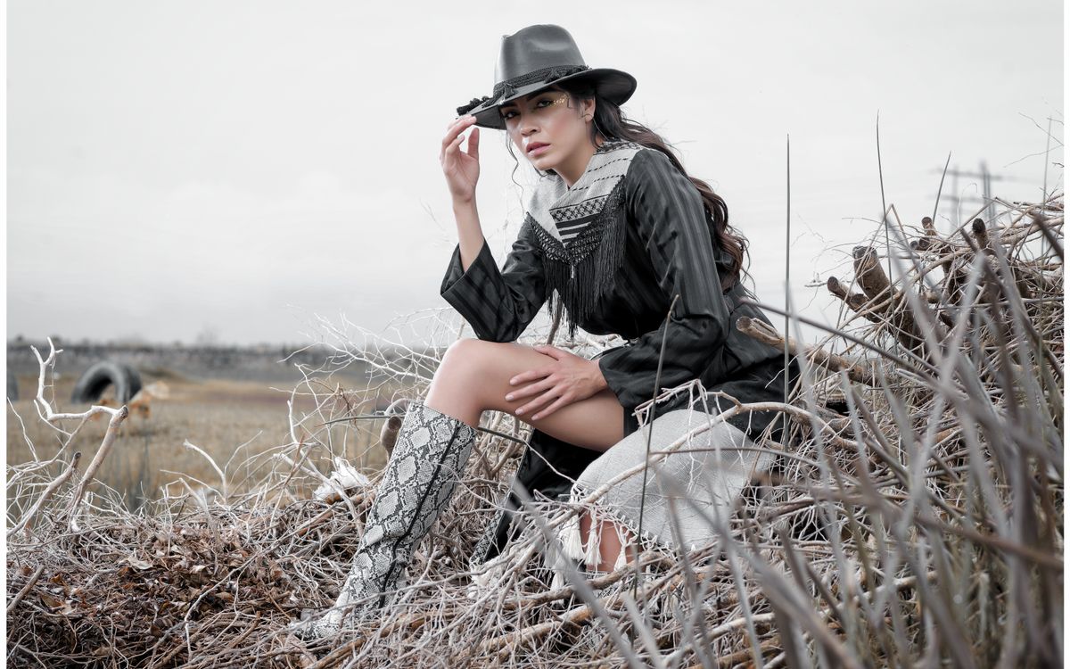 Elegancka kobieta w stroju western pozuje na zewnątrz na wiejskim polu z suchą trawą